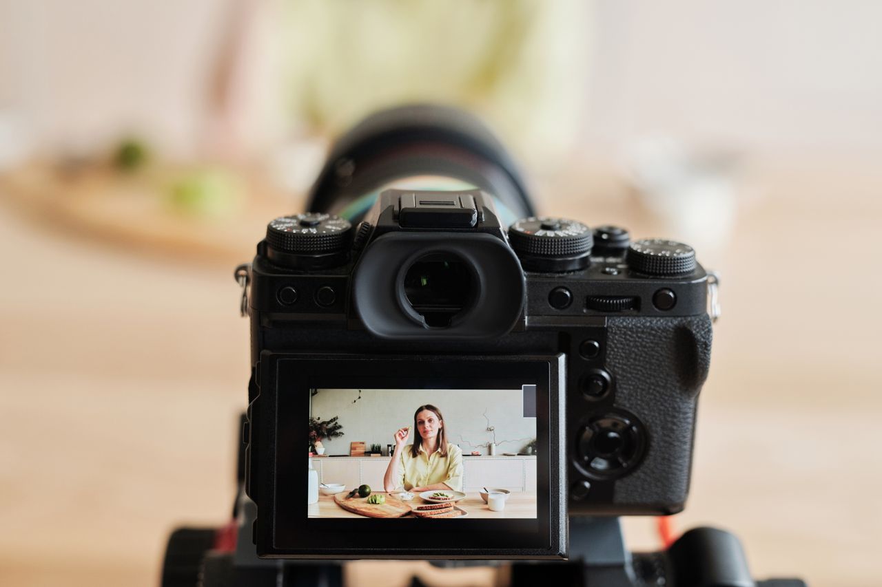Femme caucasienne faisant un vlog à la maison avec une caméra, dans un décor de cuisine, prise en intérieur.