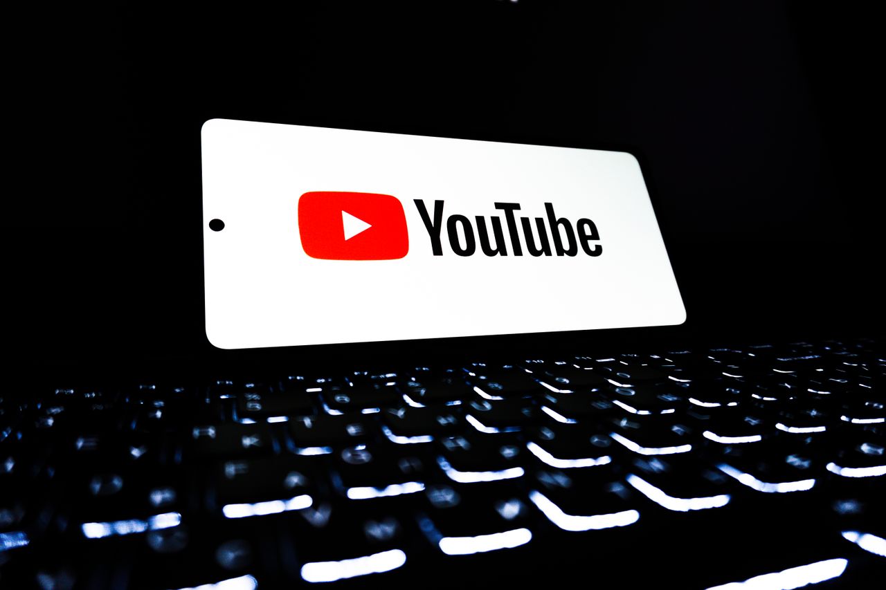 The YouTube app icon is shown on a smartphone above a backlit keyboard, suggesting digital media and online streaming.